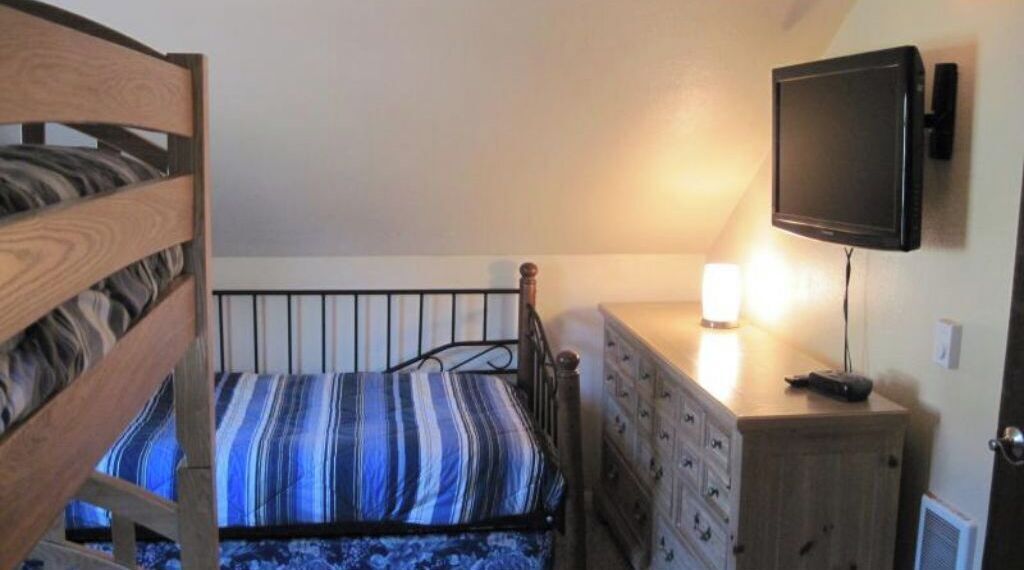 Ein Schlafzimmer mit einem Bett, einer Kommode, einem an der Wand montierten Fernseher und einer Lampe auf der Kommode.
