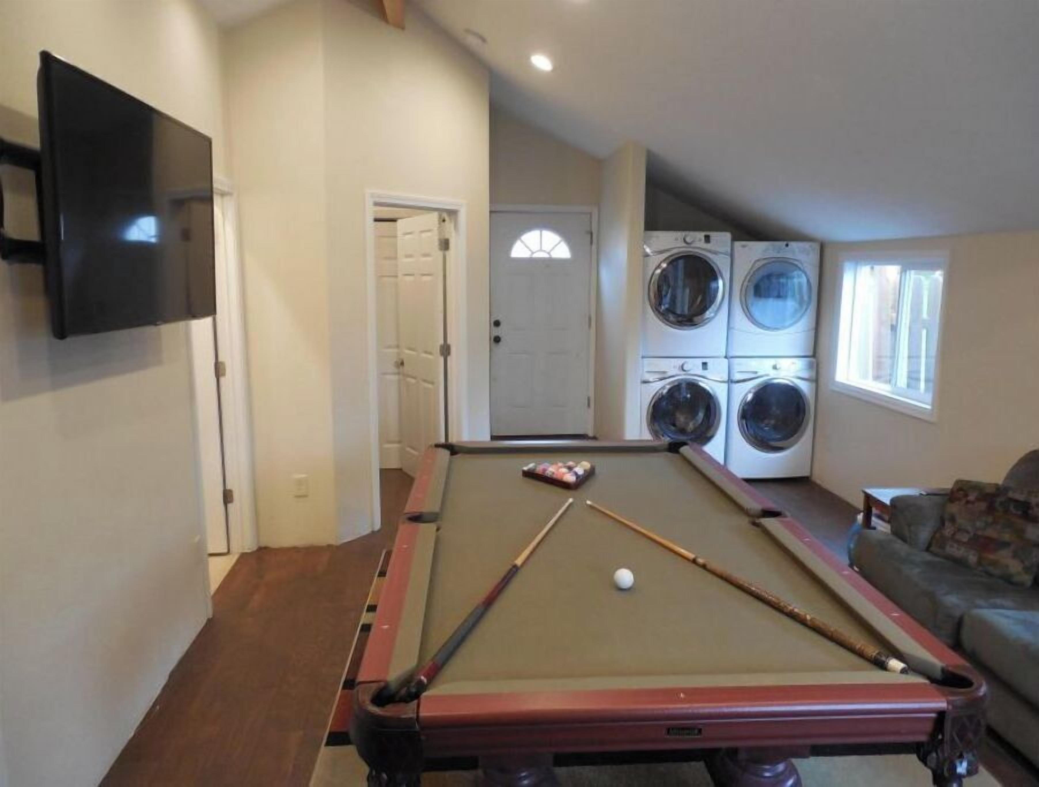 A pool table in a room with a washing machine and a television.