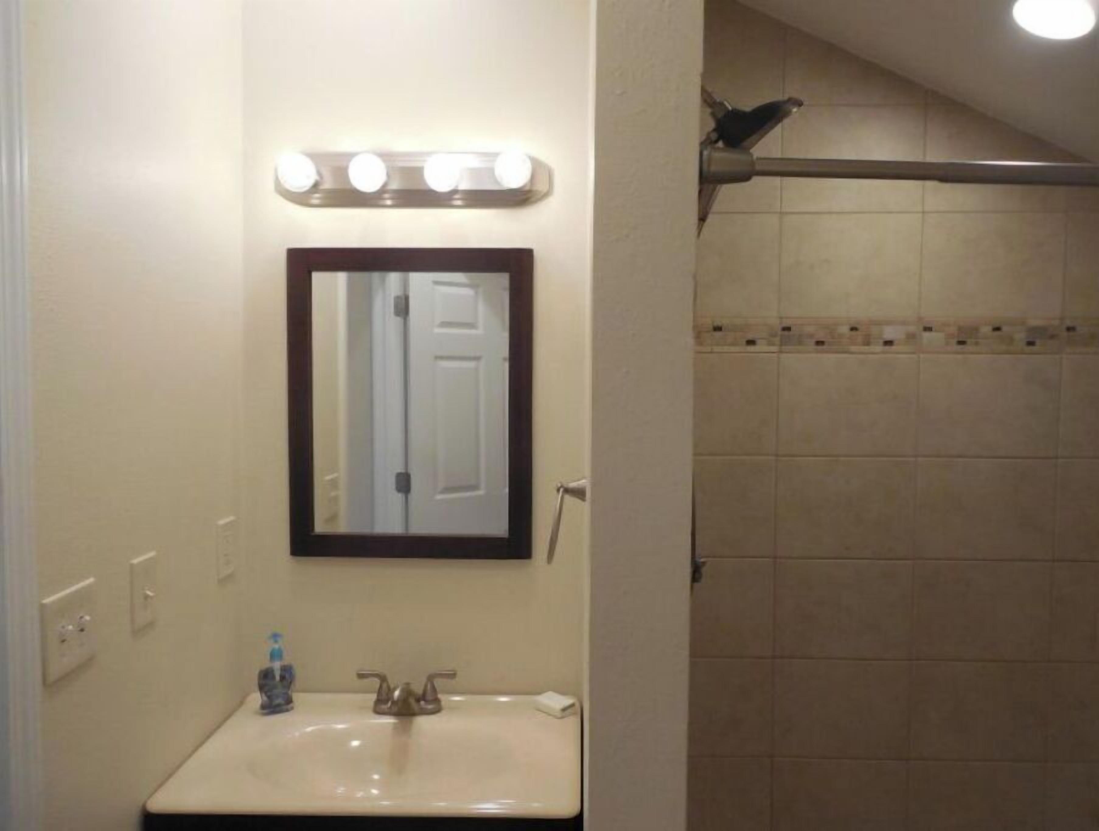 A bathroom with a sink, mirror, and a shower area.