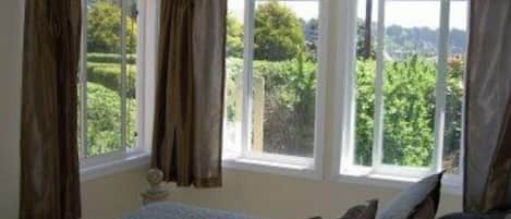 Quarto com cama, cortinas e vista para o verde lá fora.