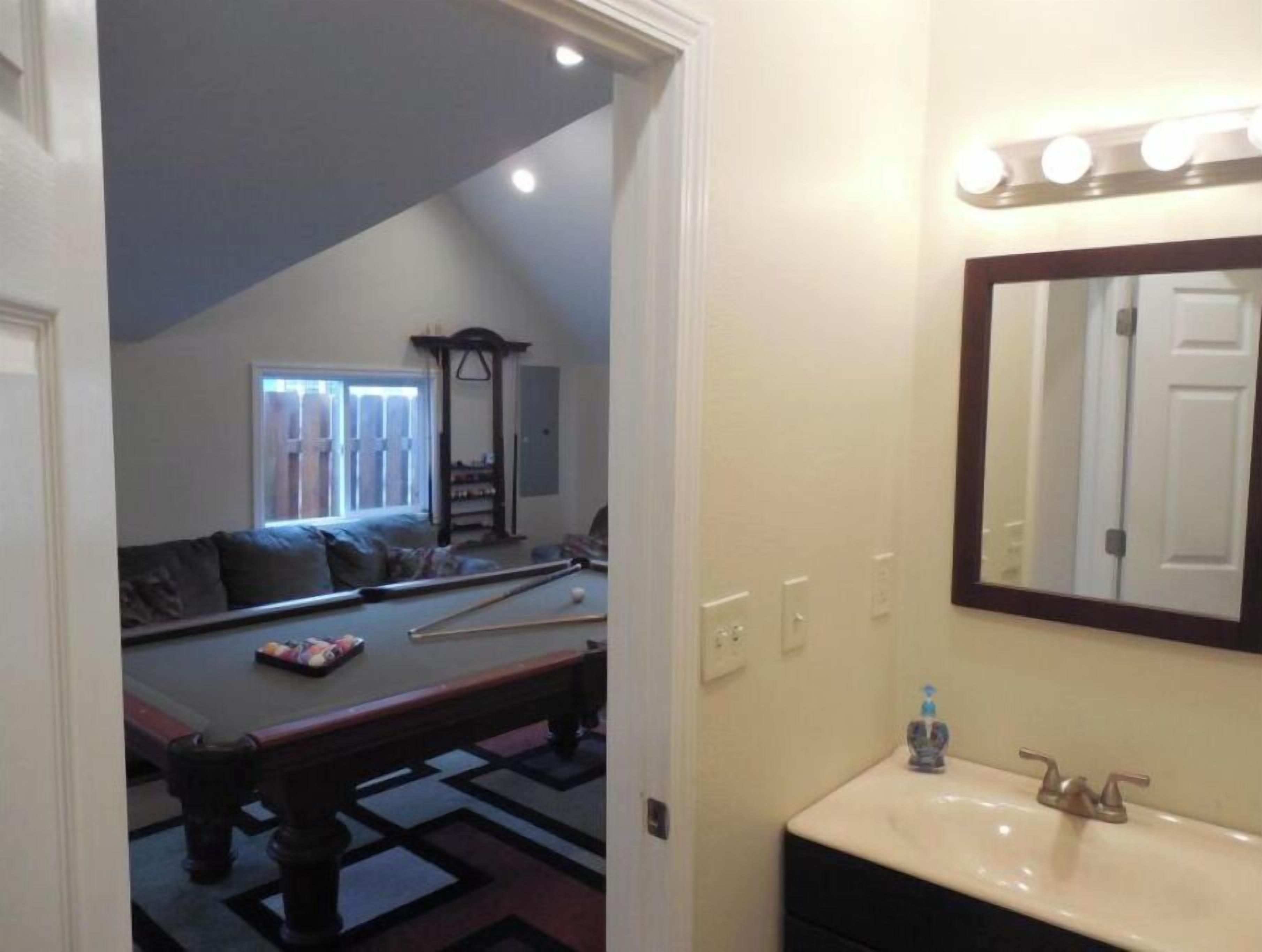 A room with a pool table, a sofa, and a mirror with lights above the sink.