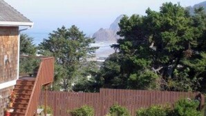 A house with a wooden staircase leading to a deck, overlooking a beach and mountains. - Beach Retreat House w/Ocean Views, Covered Hot Tub, & Large Fenced Yard (Lincoln City)