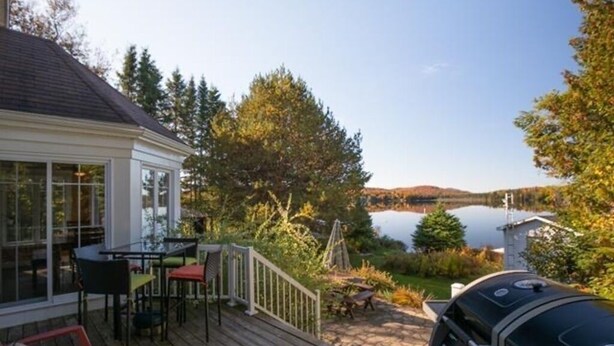 A wooden deck with outdoor furniture, a grill, and a view of a lake and hills. - Waterfront cottage Lac Quenouille (Val-des-lacs)
