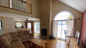 A spacious living room with a large sofa, a wooden coffee table, and a fireplace. There is a kitchen in the background with a dining area. - Waterfront cottage Lac Quenouille (Val-des-lacs)