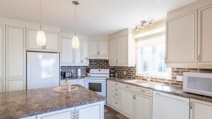 A modern kitchen with white cabinets, granite countertops, a built-in oven, and a microwave. - Waterfront cottage Lac Quenouille (Val-des-lacs)