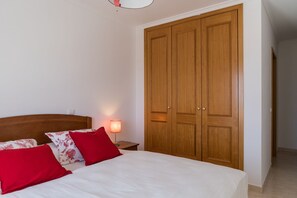 A bedroom with a bed, a nightstand, a lamp, and a wooden wardrobe.