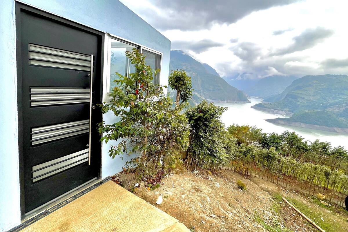 A modern building with a black door and windows, overlooking a scenic valley and a body of water.