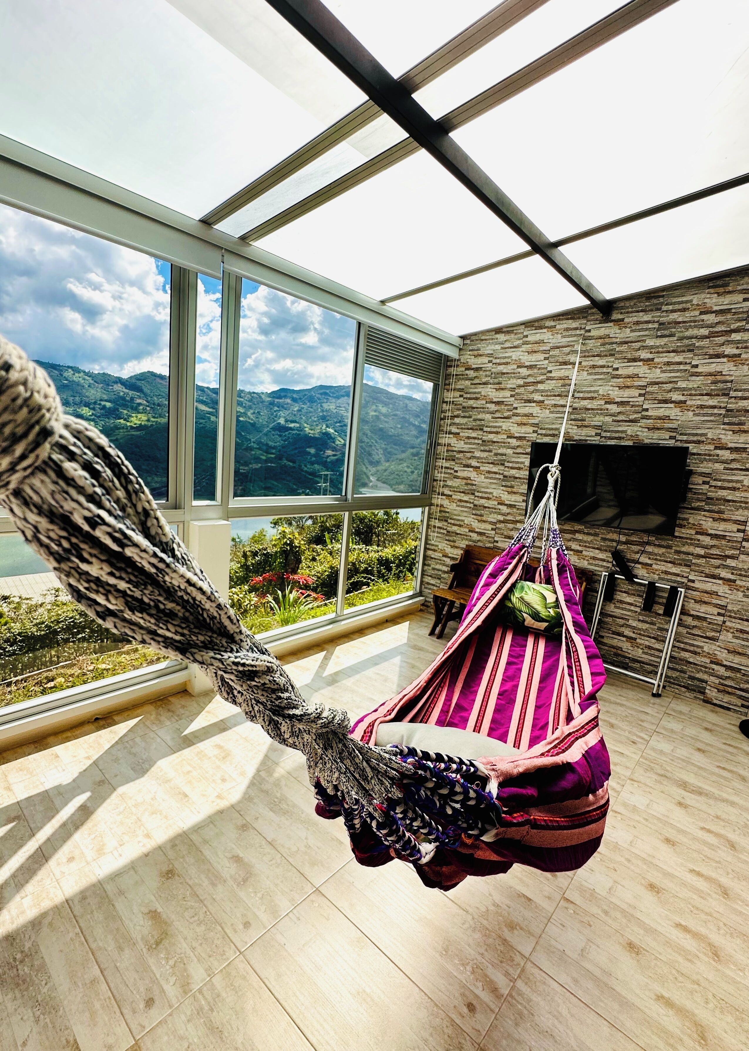 Una habitación moderna con un ventanal grande, una hamaca colgante y una pared con textura de piedra.