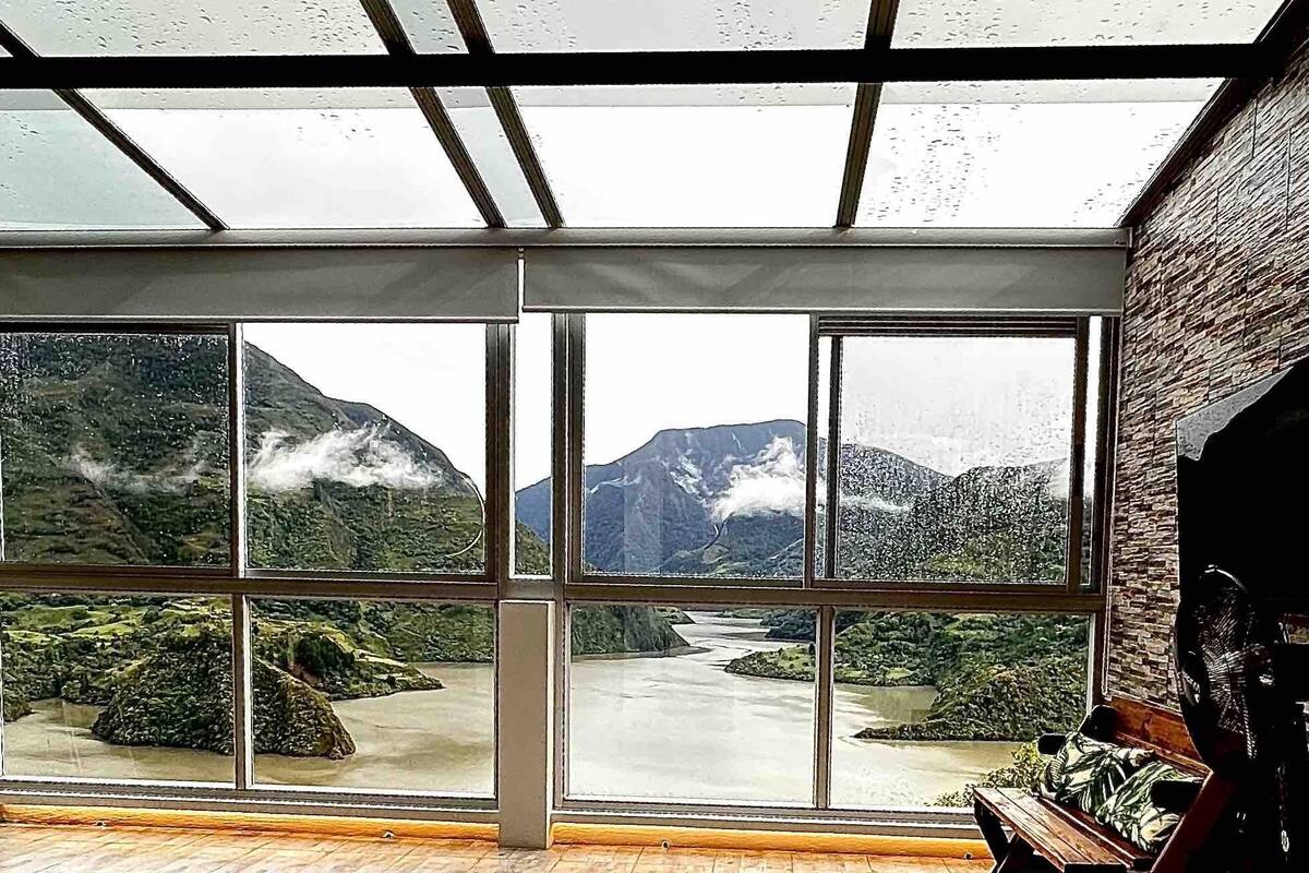 A bedroom with a large window offering a view of a river and mountains.