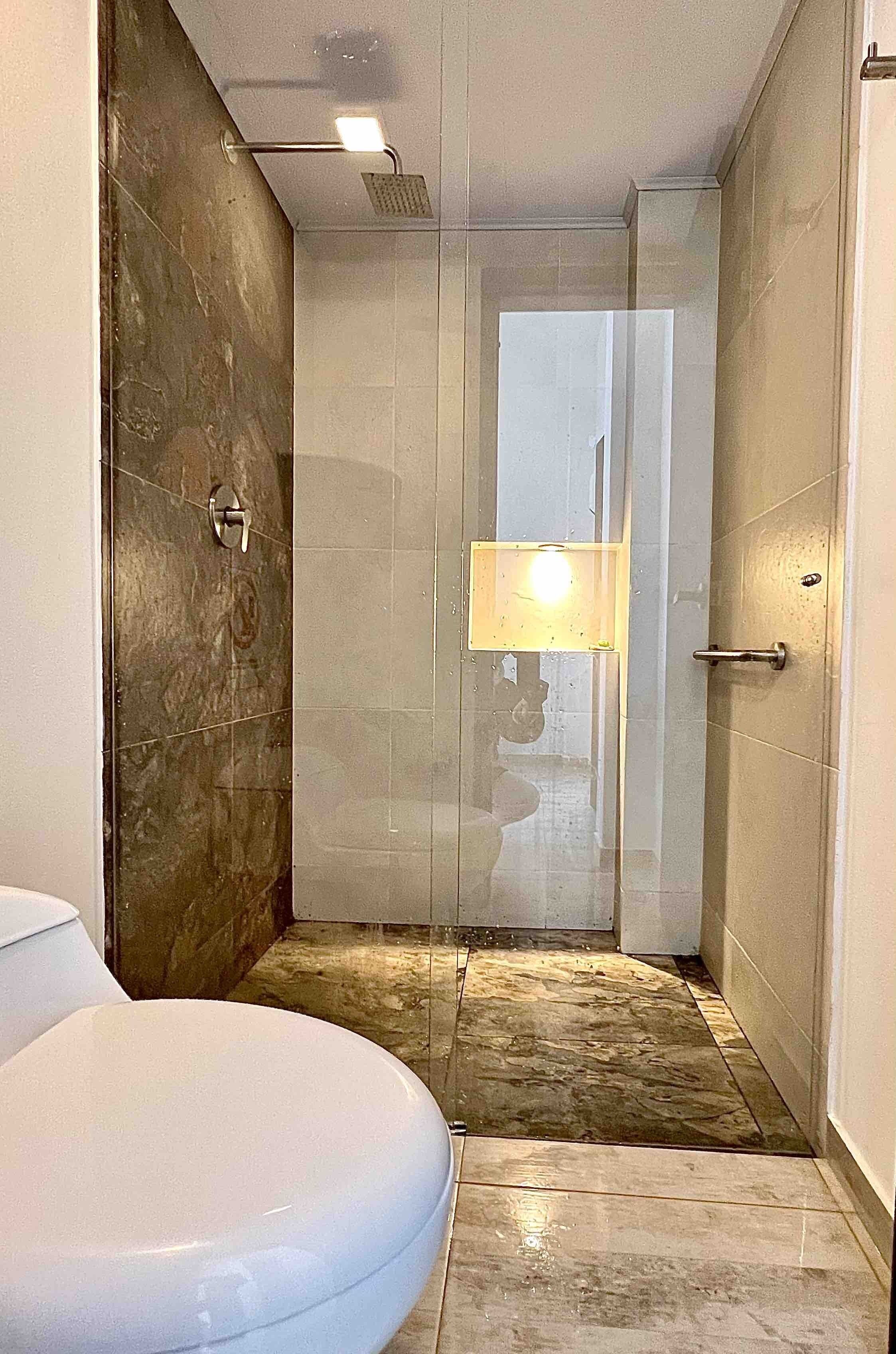 Een moderne badkamer met een douchecabine van glas, een toilet en een klein spiegel.