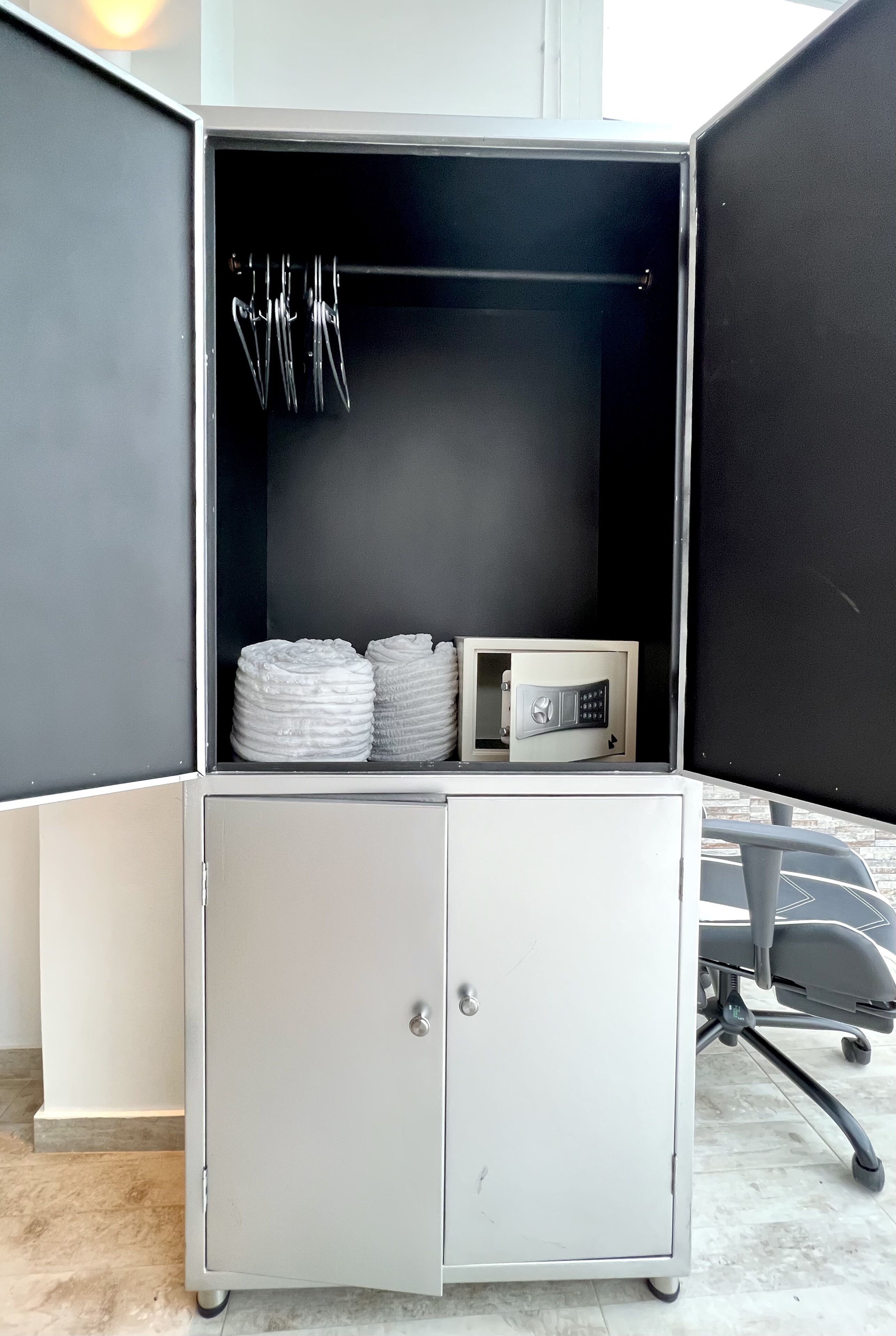 A storage cabinet with a lock, a metal rack with hooks, and two rolled-up towels.