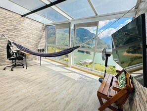 A room with a hammock, a desk, and a view of a river and mountains through large windows. - La Vista EcoHouse (Macanal)