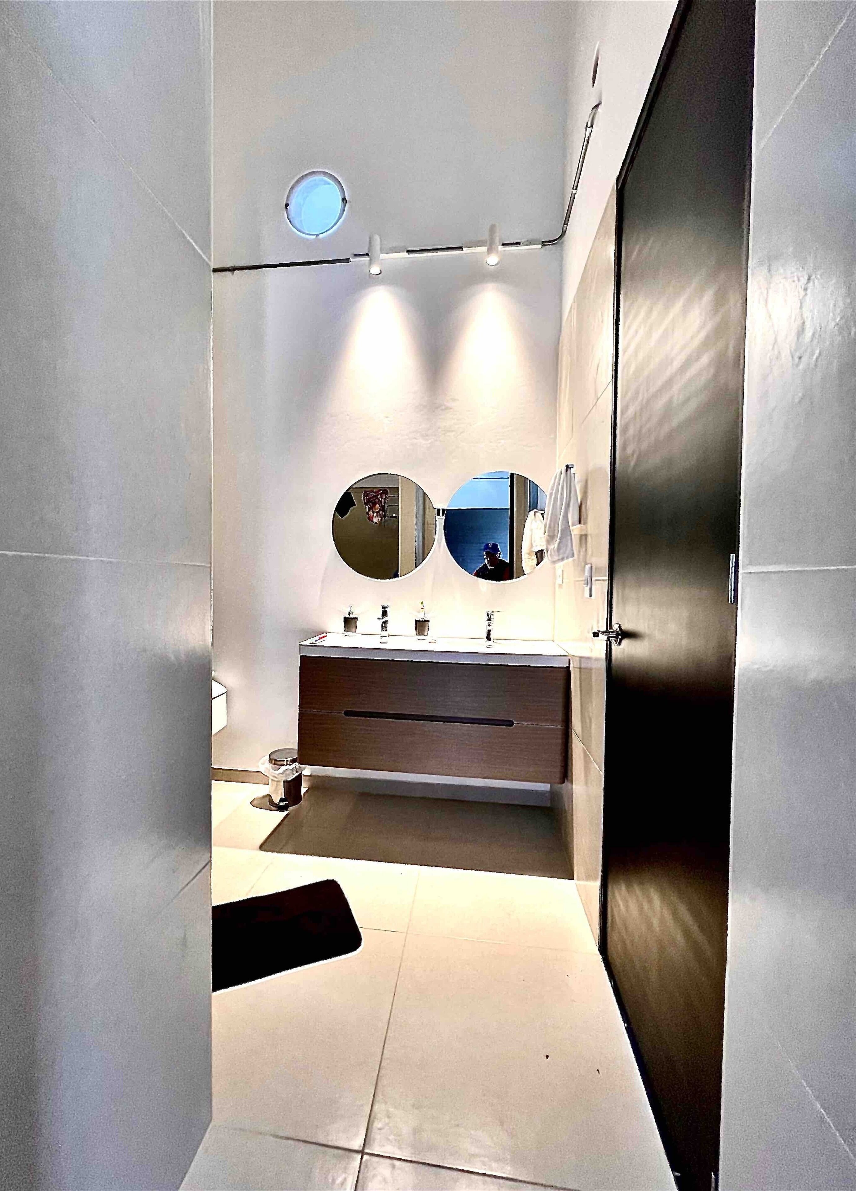 A modern bathroom with a large mirror, a vanity with a sink, and a dark door.