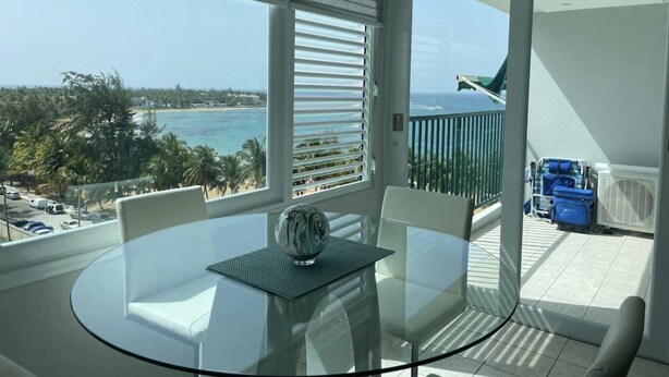 Une chambre moderne avec une table en verre, des chaises blanches et une vue sur l’océan.