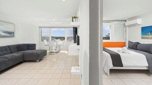 Un salon moderne avec un canapé d’angle gris, une table basse blanche et un coin repas comprenant une table et des chaises blanches.