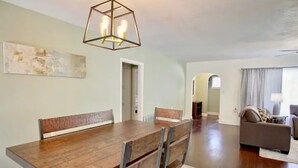 Zona pranzo con tavolo e sedie in legno, lampadario e un quadro appeso al muro.