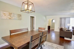 A dining area with a wooden table and chairs, a hanging light fixture, and a painting on the wall.
