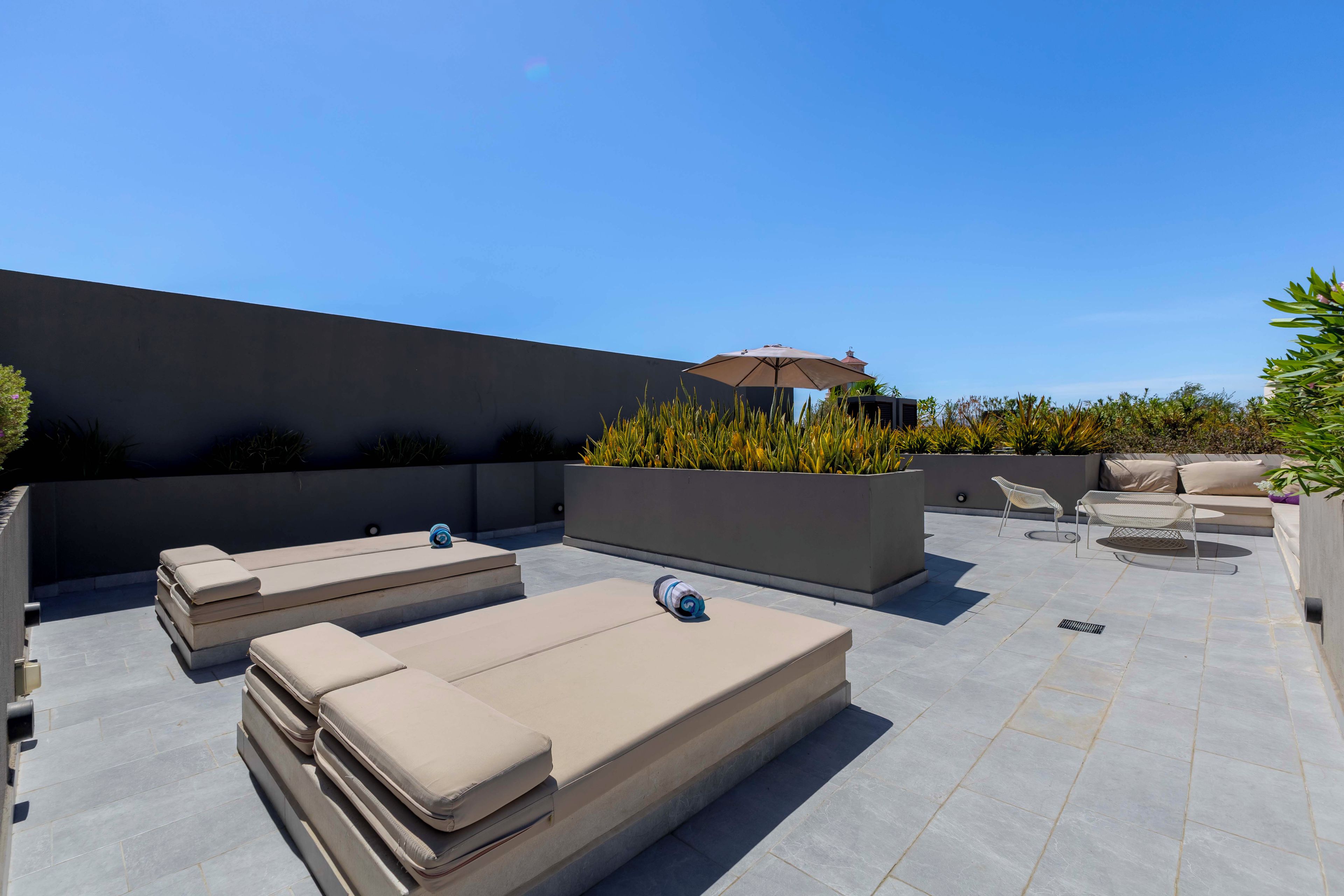 An outdoor patio with lounge chairs, a seating area, and a planter with plants.