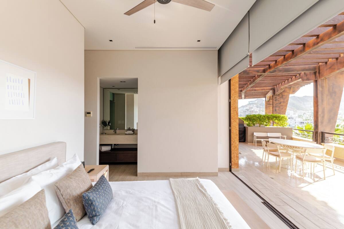 Une chambre d’hôtel moderne dotée d’un grand lit, d’un ventilateur de plafond, d’un balcon avec coin salon extérieur et offrant une vue sur la ville.