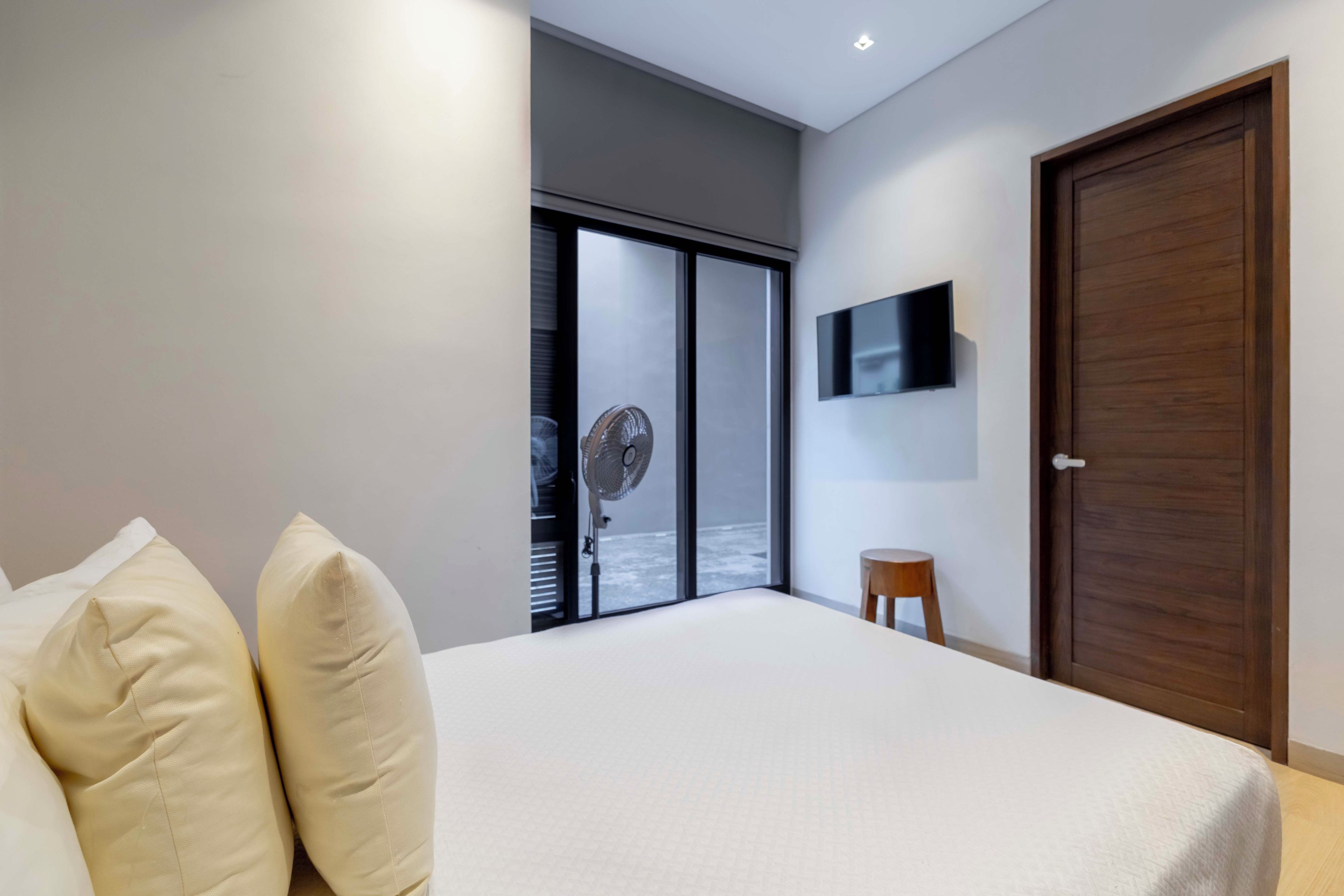 Une chambre moderne avec un grand lit, un téléviseur fixé au mur et une porte-fenêtre coulissante donnant sur un balcon.