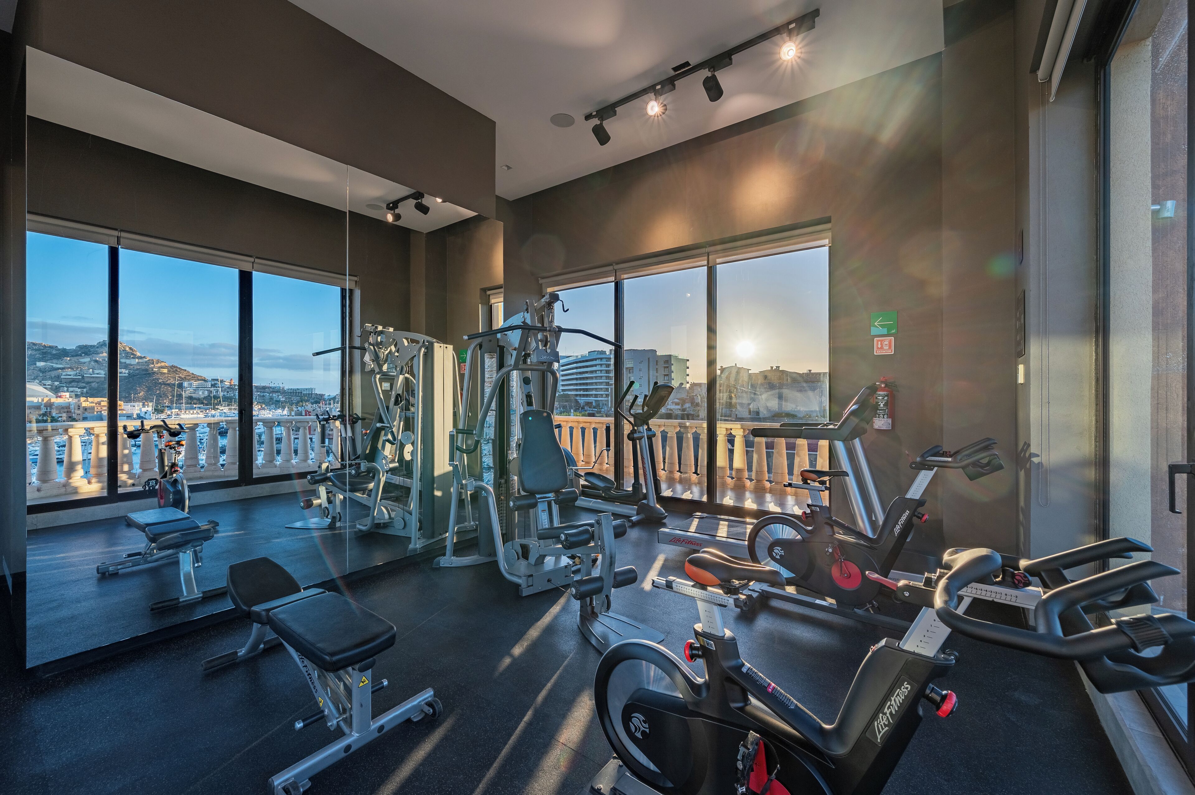 A gym with various exercise equipment, large windows, and a view of a cityscape.