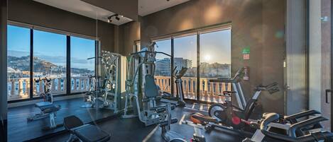A gym with various exercise equipment, large windows, and a view of a cityscape.