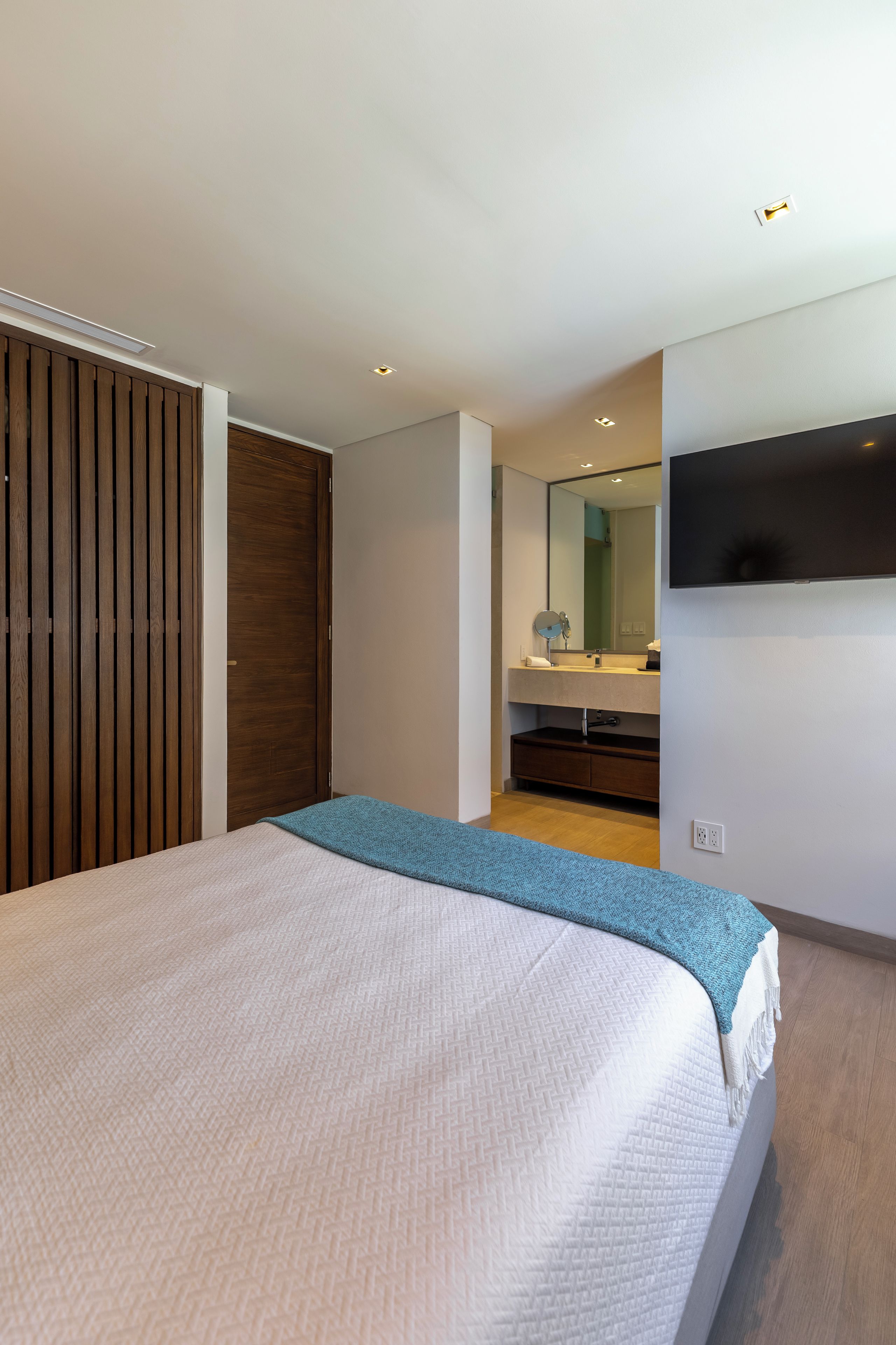 Un dormitorio moderno con una cama grande, un armario de madera y un baño con espejo y lavamanos.