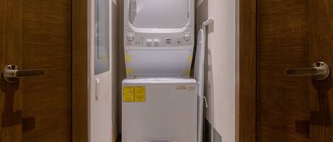 A compact laundry room with a washing machine, dryer, and a pet bed.