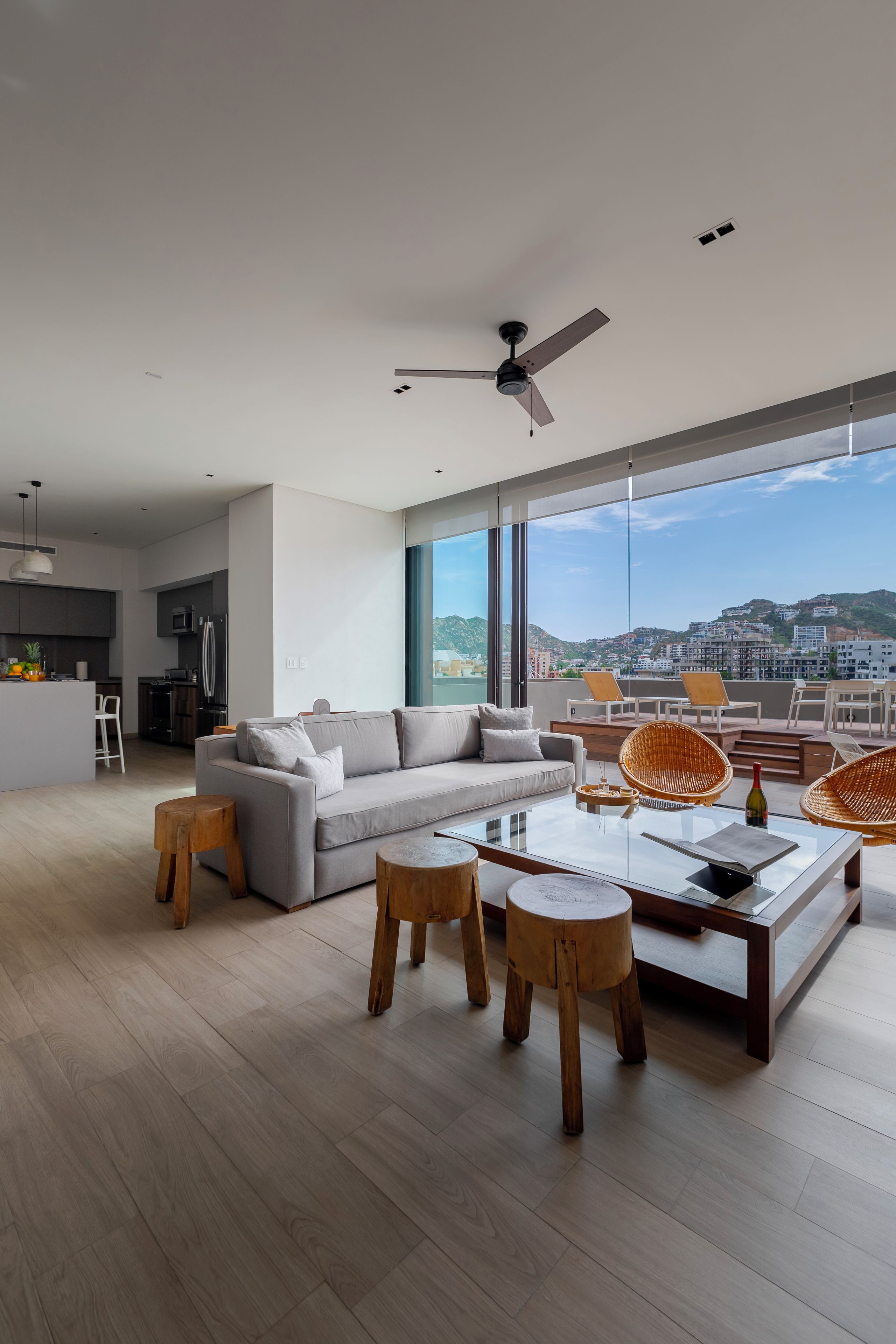 A modern living room with a large window, a ceiling fan, and a view of a cityscape.