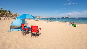 Ein Strand mit einem Zelt, roten Stühlen und freiem Blick auf das Meer und Boote.