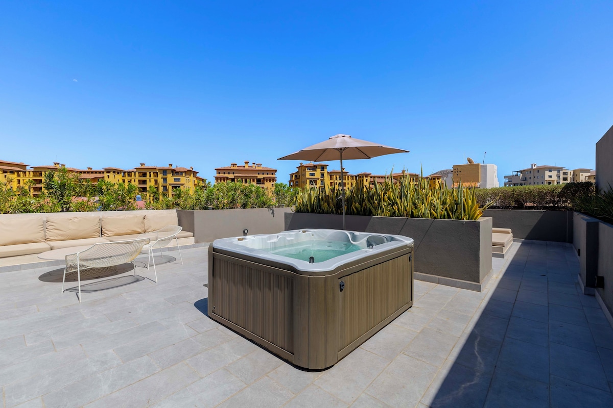 Une terrasse sur le toit avec un jacuzzi, des sièges extérieurs et une vue sur des bâtiments aux façades jaunes.
