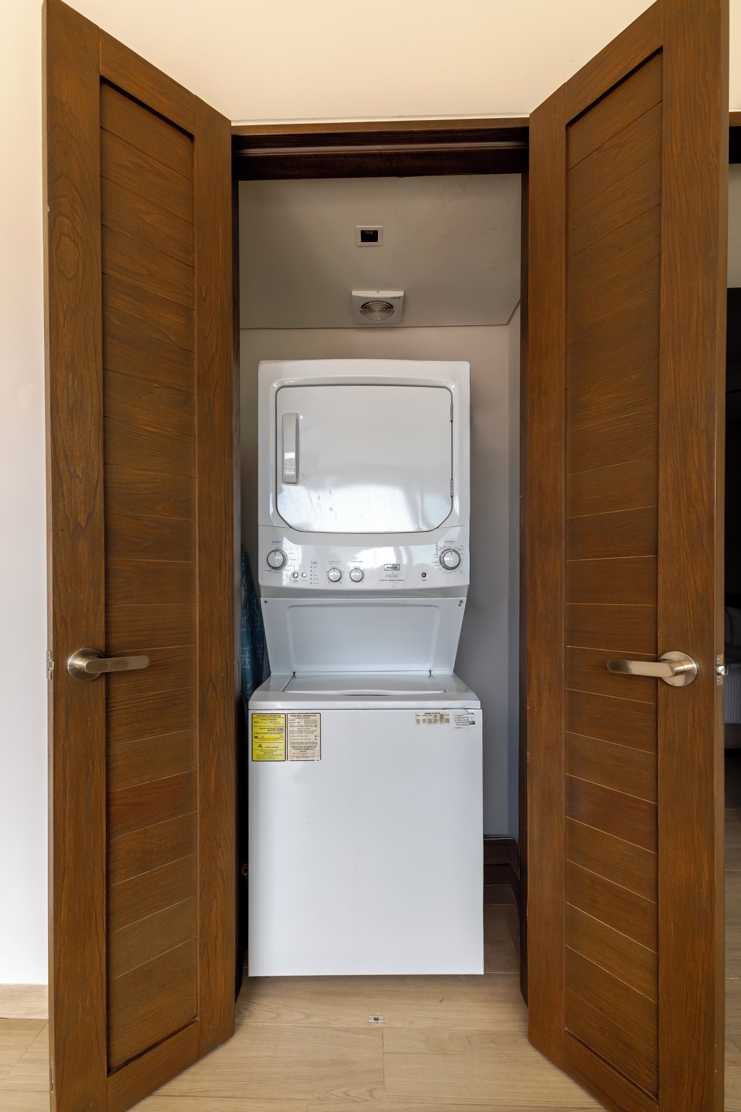 Un lavadero pequeño con lavadora y secadora de carga frontal, puertas de madera y un respiradero en el techo.