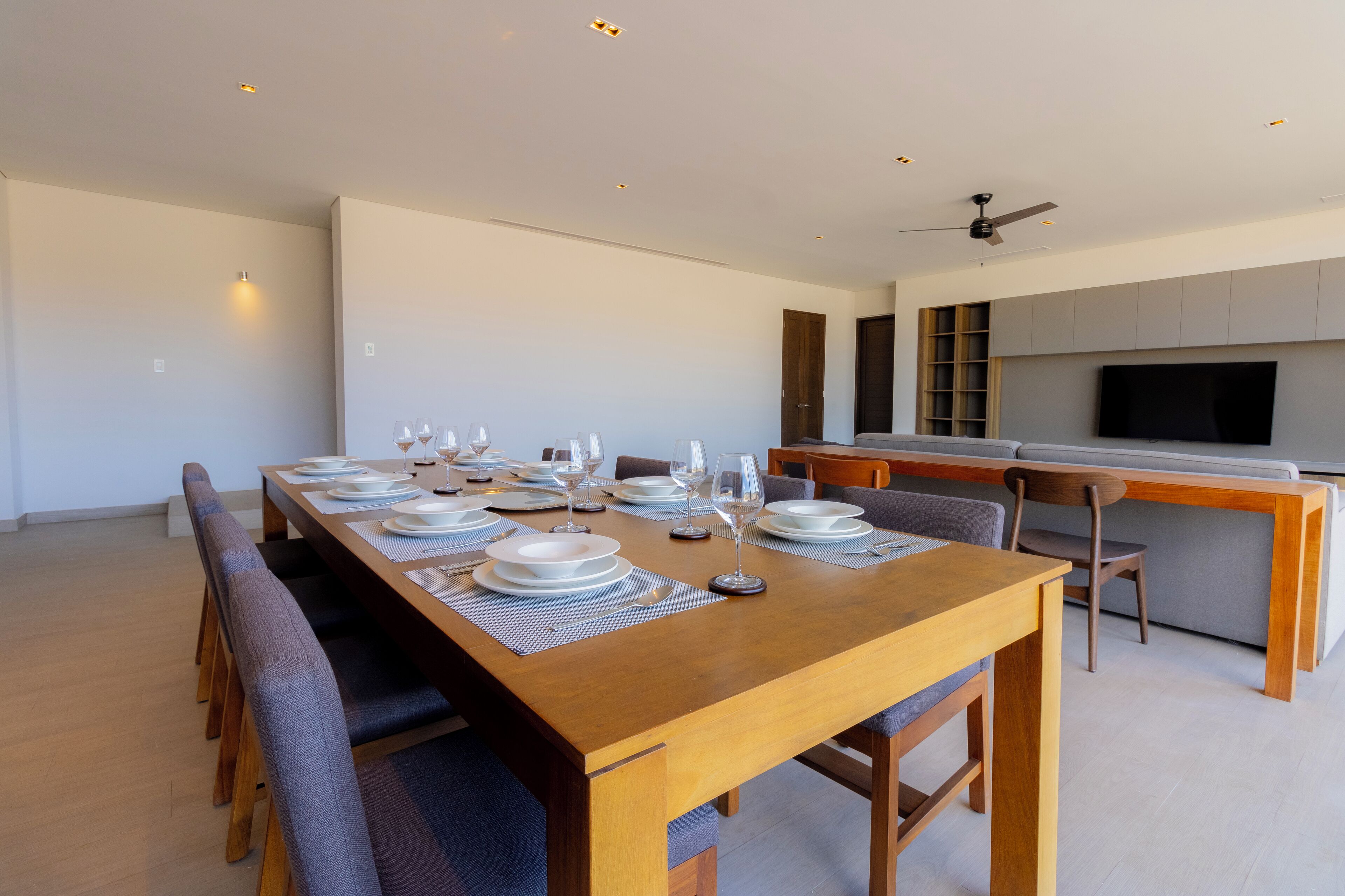 Un espace de salle à manger moderne, avec une longue table en bois dressée pour six personnes, entourée de chaises rembourrées.