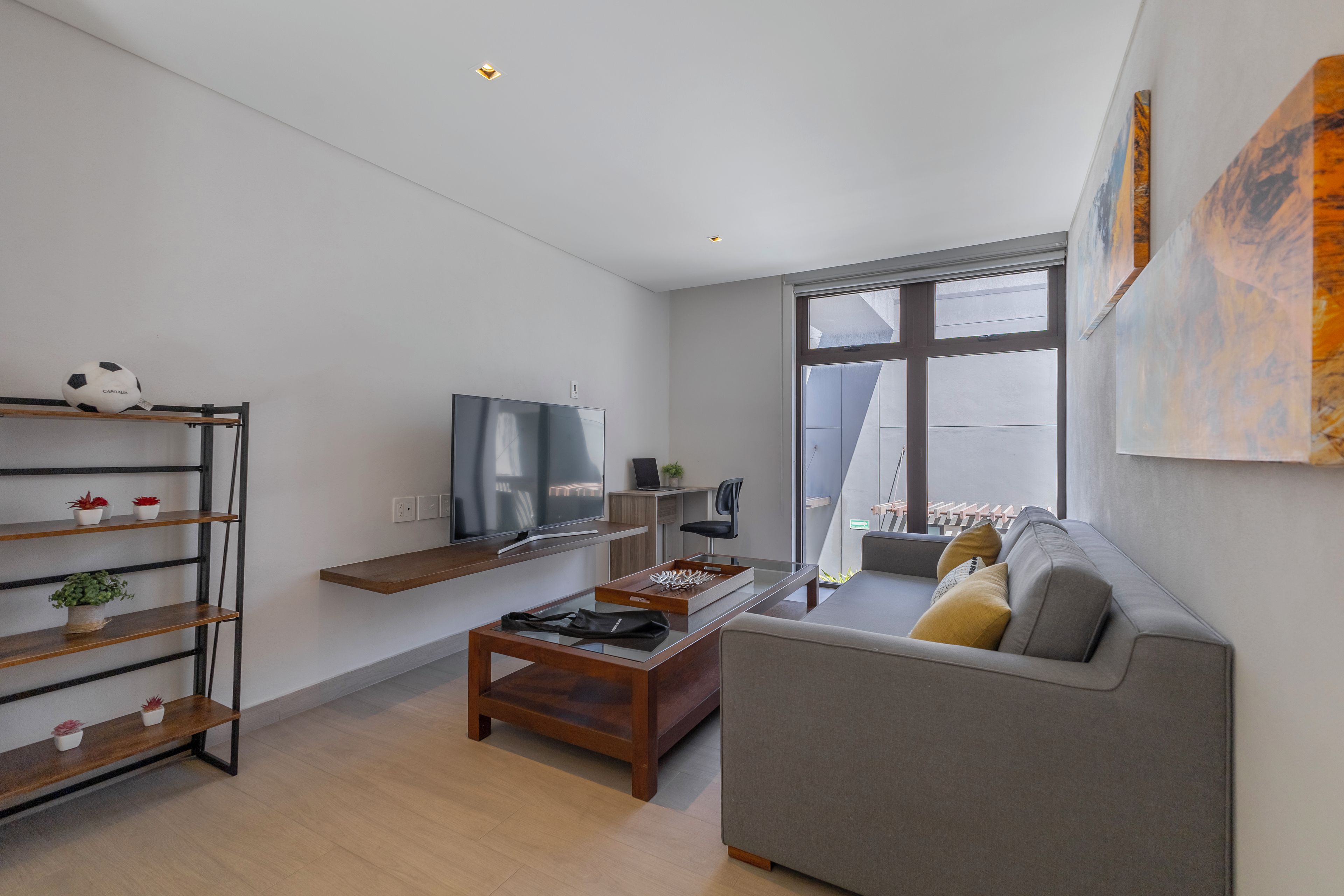 Een moderne woonkamer met een flatscreen televisie, een houten salontafel, een grijze bank en een wandplank met planten.
