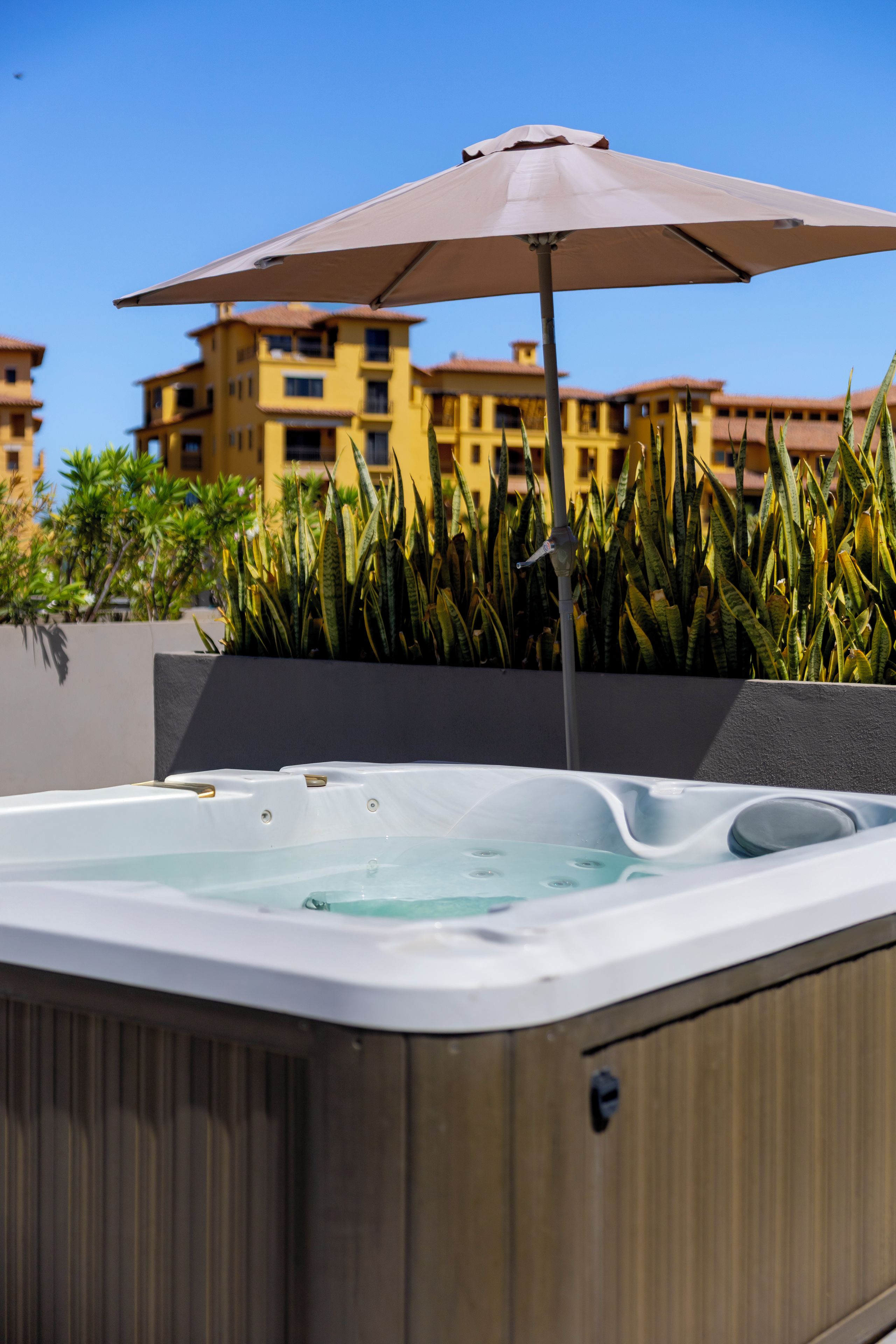 A hot tub with a metal frame, surrounded by plants and an umbrella.