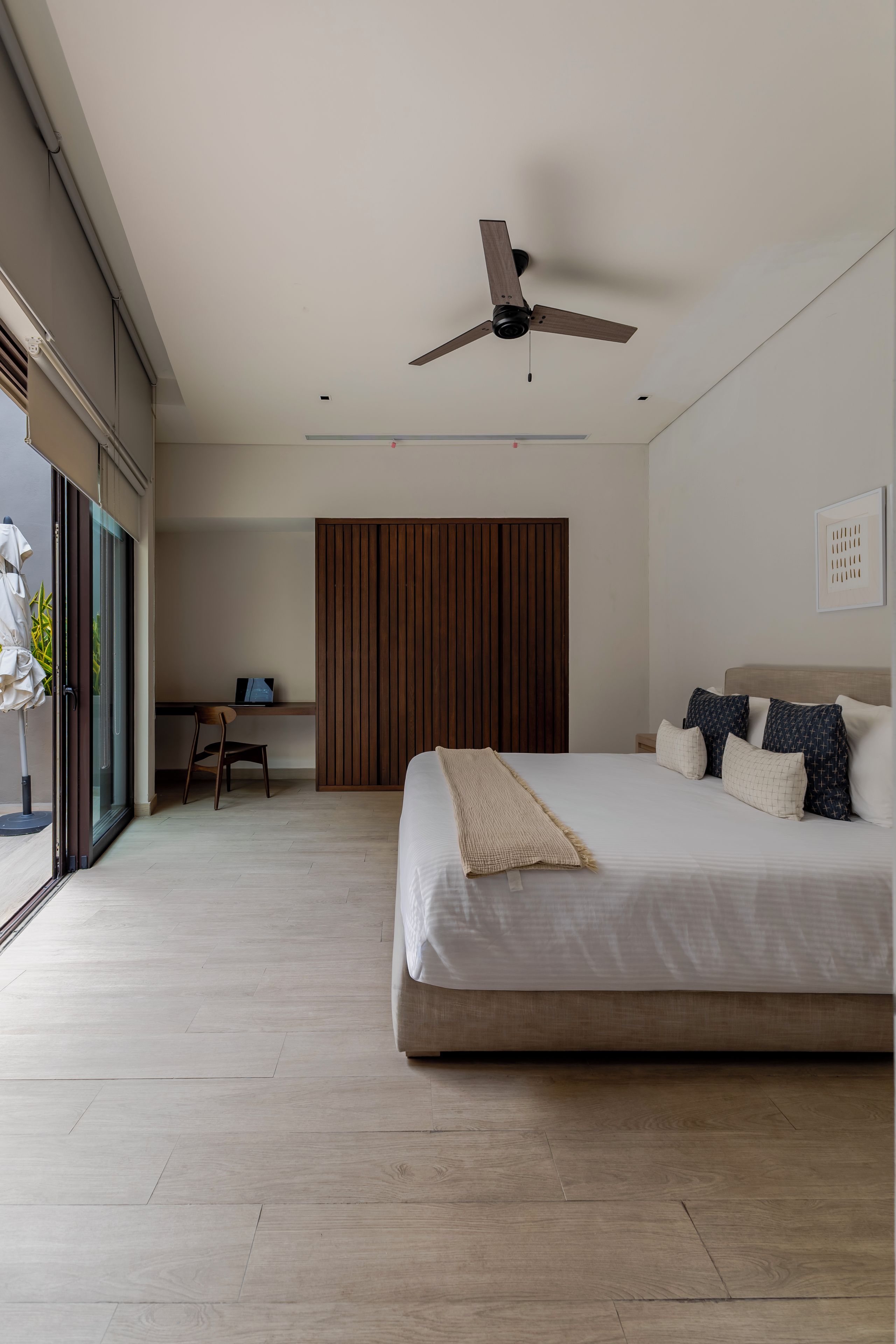 A modern bedroom with a large bed, a ceiling fan, and a desk with a chair.