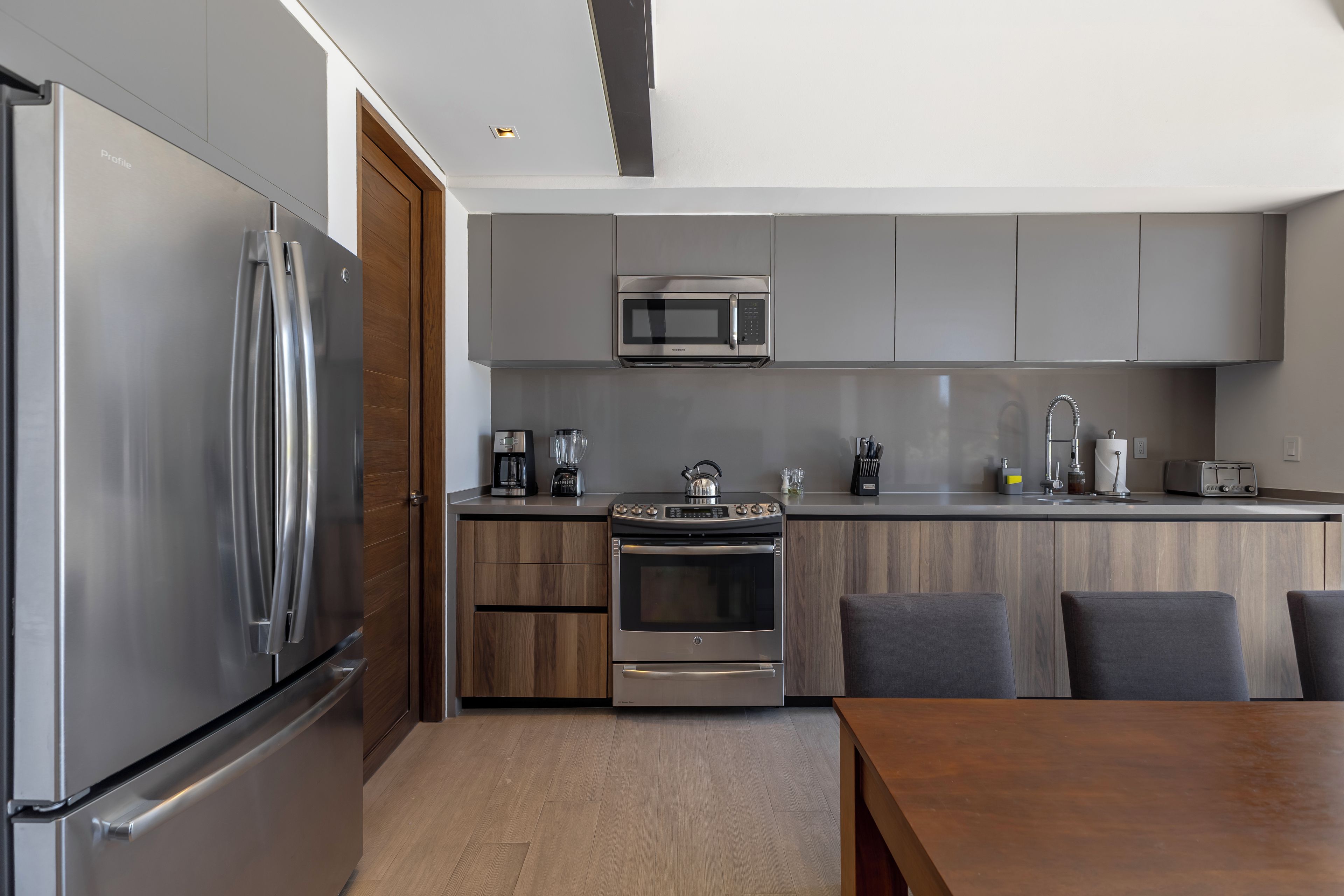 A modern kitchen with stainless steel appliances, wooden cabinets, and a dining area with a wooden table and chairs.