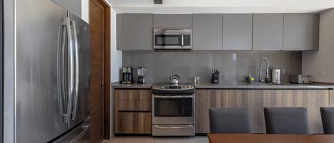 A modern kitchen with stainless steel appliances, wooden cabinets, and a dining area with a wooden table and chairs.