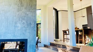 Un interior moderno con chimenea de hormigón, vigas de madera y zona de comedor con sillas y una mesa.