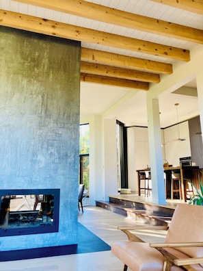 A modern interior with a concrete fireplace, wooden beams, and a dining area with chairs and a table.