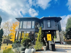 A modern two-story house with large windows, a stone base, and a yellow door.