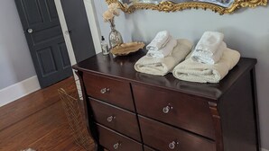 Un dormitorio con un espejo grande y ornamentado, un aparador de madera oscura con toallas, una alfombra mullida y una ventana con cortinas.