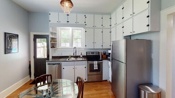 Una cocina moderna con armarios blancos, electrodomésticos de acero inoxidable y una mesa de comedor de vidrio.