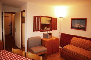 A compact room with a bed, a desk with a computer, a chair, and a dining table with a checkered tablecloth.
