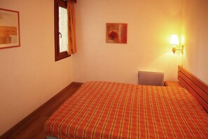 A room with a bed, a window with curtains, a wall-mounted lamp, and a framed picture.