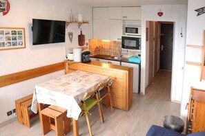 A compact kitchen with a microwave, kettle, and sink. There is a dining table with benches and a TV mounted on the wall.