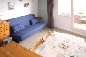 A room with a blue sofa, wooden dresser, and a dining table with chairs.
