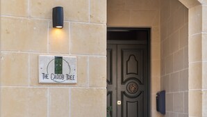 Un mur de pedra amb un rètol que diu “The Carob Tree” i una porta amb un disseny decoratiu.