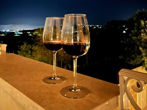 Two wine glasses on a balcony with a city view at night.