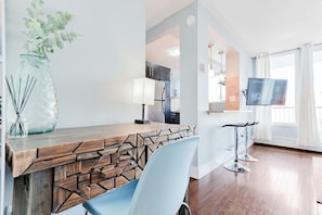 Una sala de estar moderna con una mesa de centro de madera, un sillón azul, un televisor montado en la pared y un gran ventanal con cortinas.